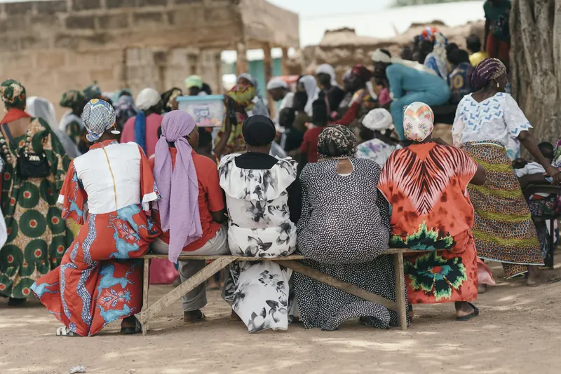 Villagers seated on benches at an outdoor community gathering